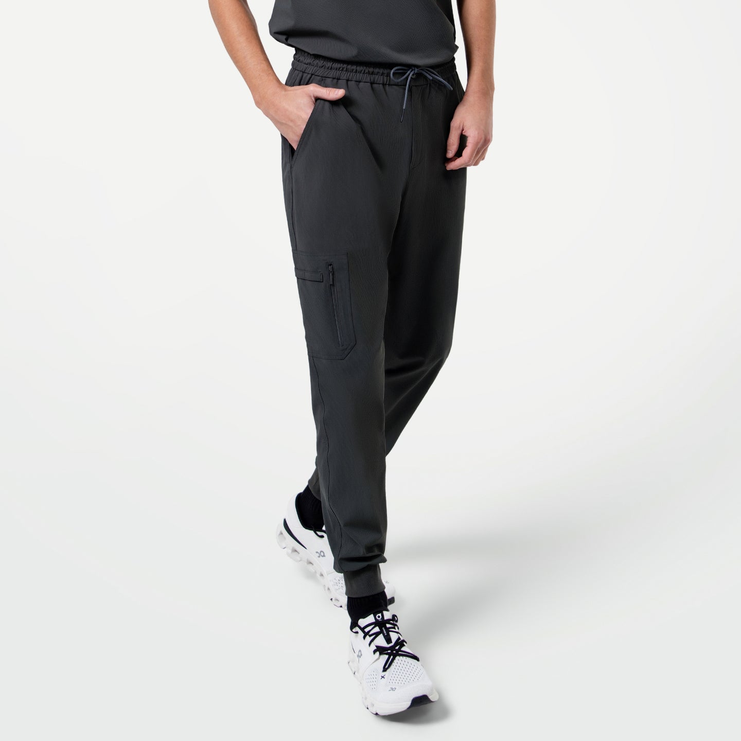 Image of Male model in mid-step with one hand in his pocket, showcasing Zipper Pocket Jogger Scrub Pants in Deep Gray paired with a matching scrub top and white sneakers.